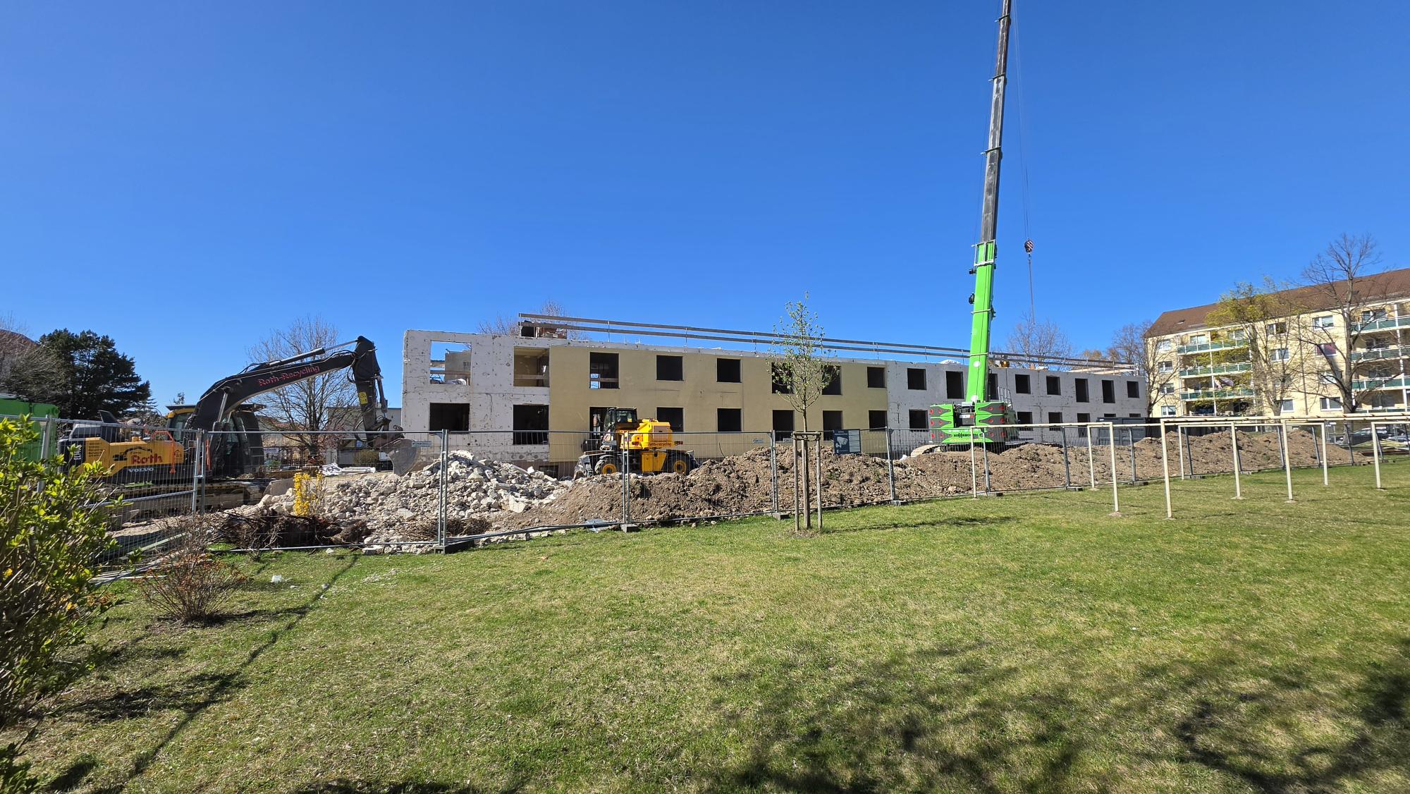 Baustelle vor einem Wohngebäude welches sich im Rohbau befindet, Kran und Baumaterialien im Vordergrund